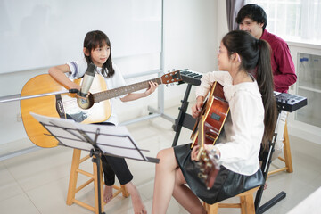 teen asian girls take guitar lesson in a music tutoring,elementary age students learning a new skill music during school break