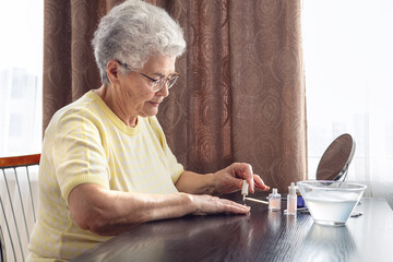 Elderly woman with gray hair wearing glasses 70+ years old doing her own manicure at home, Self-care theme, beauty and self-care, self-love, independence and aging with grace