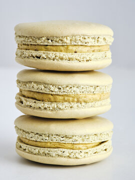 Three delectable macarons of light hue are stacked neatly, showcasing their smooth, delicate shells and creamy filling. This elegant arrangement highlights the artistry of pastry making