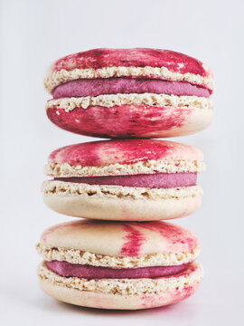 A stack of three macarons showcases a vibrant red design with raspberry filling. The desserts are arranged neatly, highlighting their delicate texture and colors