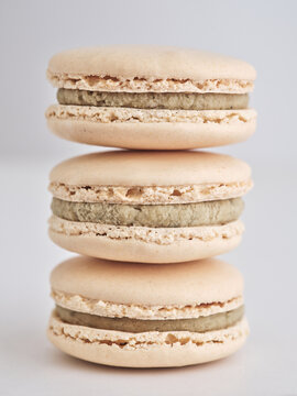 Three carefully stacked macaroons showcase their smooth texture and earthy green filling. The soft pastel colors emphasize their delicate design and appealing look