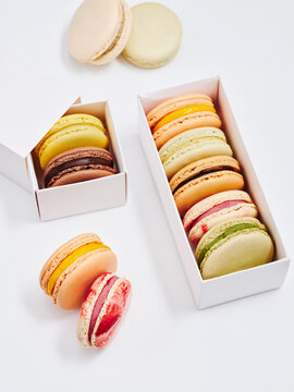 Assorted macarons in various colors and flavors are neatly arranged in two stylish boxes. The setting is clean and minimal, highlighting the delicate treats