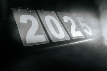 Monochrome calendar displaying 2025 with bold white numbers on dark pages, surrounded by smoky mist on a dark background. A sleek and minimal futuristic design.