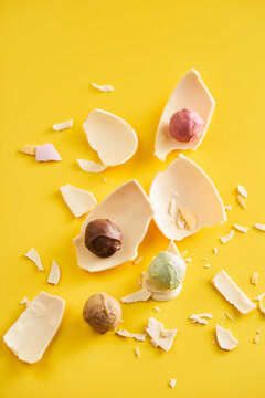 Various ice cream scoops in pastel colors rest within broken chocolate egg shells on a vibrant yellow surface, creating a playful and appetizing decor