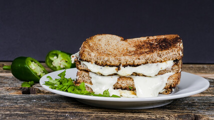 Delicious melted cheese sandwich with jalapenos on plate on rustic table with black background