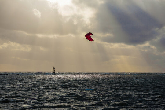 
A kitesurfer riding the sea using the power of the wind, with a ship and a sky with clouds behind him.
