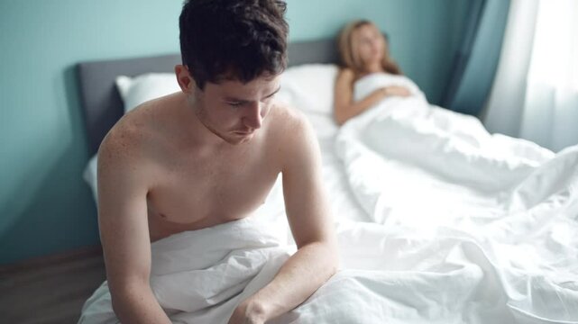 Frustrated man sitting on bed on different side of woman. Young unhappy couple having problem in bedroom, quarrel between lovers. Divorce, marriage, conflict, family crisis, love concept.