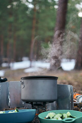 Steam comes out of a pot of boiling water, cooking on a gas burner in conditions of autonomy while hiking in the forest
