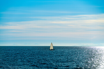 Small sailboat in backlight sailing in the ocean