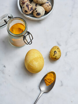 A jar filled with turmeric powder sits alongside vibrant quail eggs, one of which is cracked open. The countertop is made of smooth marble, creating a warm and inviting atmosphere