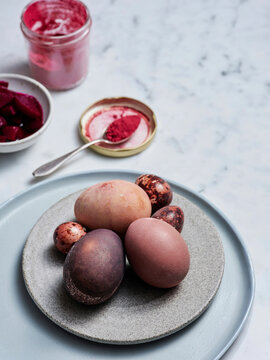Dyes create a stunning palette on eggs placed artistically on a circular plate. Surrounding items include bowls of vibrant beetroot and creamy yogurt, showcasing a creative culinary display