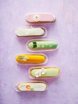 A vibrant selection of elaborately designed pastries arranged on a purple surface. Each piece features unique colors and decorative elements, showcasing skilled baking artistry