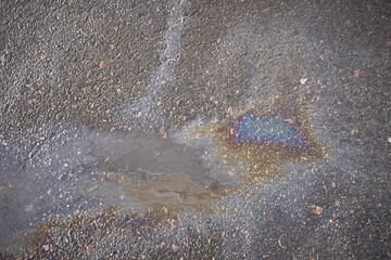 An oil leak creates colorful designs on the asphalt surface, highlighting the issue of pollution and posing a road safety risk.