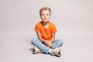 Little boy listening to music on light grey background