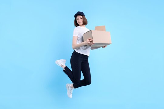 Happy postwoman with parcel jumping on light blue background