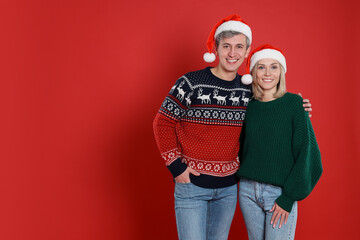 Fototapeta premium Happy couple in Santa hats on red background, space for text. Christmas celebration