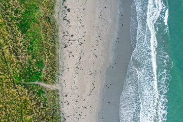A serene top-down view of an Irish beach, showcasing gentle waves meeting the sandy shore and lush coastal grasslands