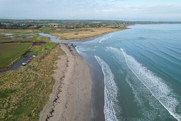 A sweeping aerial view of Ballynamona Strand Beach in Ireland, showcasing its expansive sandy shoreline, gentle waves, and lush coastal surroundings from above.