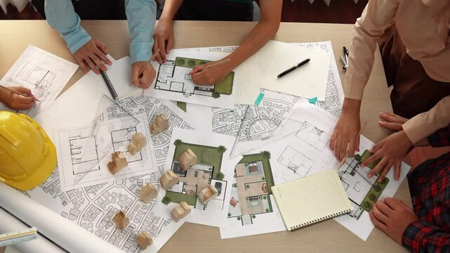 Architect and safety engineer discussion about building construction use blueprint on table with architectural document, measurement tool and wooden block scatter around at modern office. Delineation.