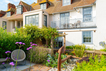 Picturesque back garden showing lush shrubs in front of seaside terraced houses on the Suffolk coast in England. Some patio furniture is visible in the frame.