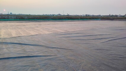 A farmer produces salt manually by evaporating seawater in shallow ponds. This traditional method, involving natural sun and wind, yields high-quality salt crystals prized for their purity.