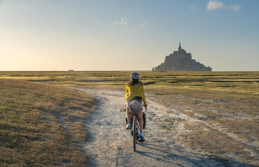 Bike and adventure in Mont Saint Michel. Female traveler pedals through rural area, in the background is the famous Mount Saint Michel.