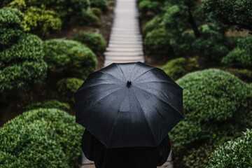 静かな庭で黒い傘を持つ人物が小道を歩いている様子
