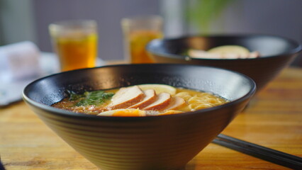 A delicious ramen topped with a soft egg and tender chicken meat is served in an ornate bowl on a warm wooden table.