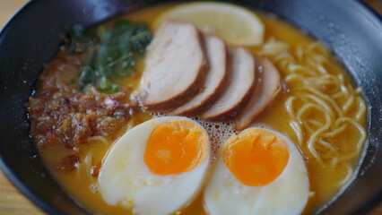 A delicious ramen topped with a soft egg and tender chicken meat is served in an ornate bowl on a warm wooden table.