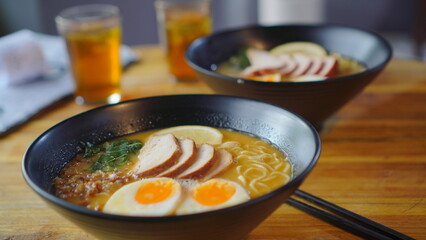 A delicious ramen topped with a soft egg and tender chicken meat is served in an ornate bowl on a warm wooden table.