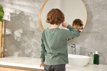 Cute boy brushing his teeth near mirror in bathroom, back view