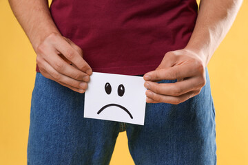 STD (sexually transmitted diseases). Man holding sticky note with drawn sad face on yellow...