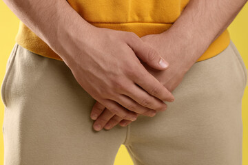STD (sexually transmitted diseases). Man suffering from symptoms on yellow background, closeup