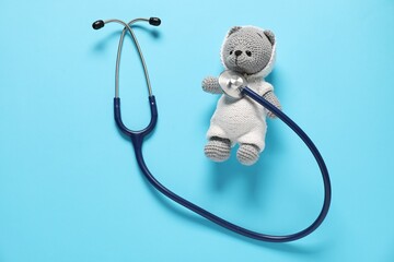 Pediatrics concept. Toy bear with stethoscope on light blue background, top view