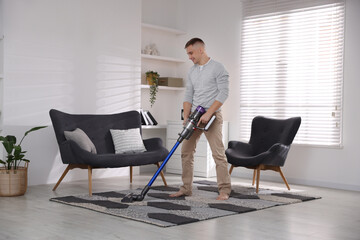 Young man cleaning rug with cordless vacuum cleaner at home