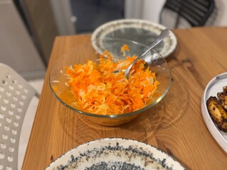 Grated carrots and radish salad in glass bowl on wooden table