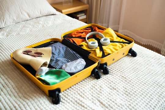 Open yellow suitcase with different family clothes and accessories on bed in light bedroom. Preparing luggage for journey, copy space. 