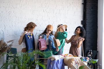 Happy women try on things at second hand store. Choose casual clothes, shoes, hats, bags, jewellery. Idea of exchange old wardrobe. Eco friendly cloth concept. Zero waste shopping, reduce and reuse