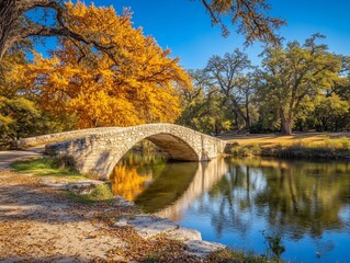 Stone arch bridge over calm river reflecting golden autumn foliage.