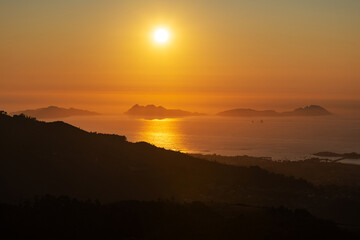 Aerial view of a vibrant orange sunset over the Ría de Vigo estuary in Galicia, Spain, with the serene Cies Islands silhouetted in the background.