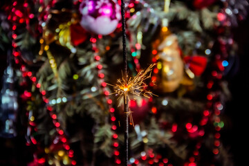 Beautiful small sparklers burn against the backdrop of beautiful beads on a Christmas tree