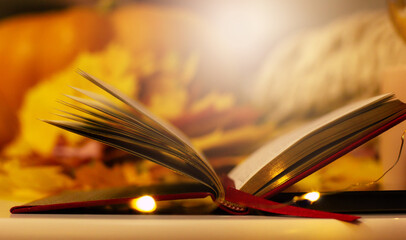This cozy autumn image features an open book with golden pages, surrounded by vibrant fall leaves,...