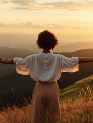 A powerful African American woman stands with arms open wide on a hilltop as the sun sets, embracing the beauty of nature and celebrating her heritage during Black History Month