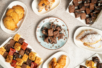 Overhead shot of assorted pastries and brownies arranged on plates and in boxes, creating an...