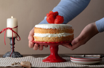 Homemade  layered cake with whipped cream and hearts of srawberry on red plate.