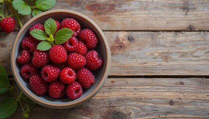 A closeup of fresh ripe raspberries in a bowl atop an aged wooden table. Background of summer berries. Blank space. Bird's-eye view
