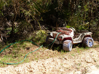 A child's toy jeep with a green garden hose coming out of the engine area and across the ground abandoned by the side of the road in the Ocala National Forest, Florida, USA. 
