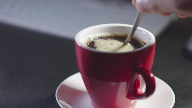 Person hand stirring coffee in a cup with spoon. Breakfast morning of a cup hot black coffee on a wooden background. footage b-roll Slow motion scene in 4K. Hand-stir coffee.