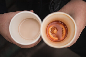 Two disposable cups with hot drinks, top view. Tea and coffee. Natural sea buckthorn tea with a slice of orange and raf. Tea or coffee. Coffee to go. Tea to go. Outdoor recreation.