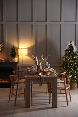 Christmas table setting with stylish dishware, glasses and burning candles in festive decorated room